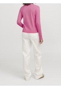 Pull ajusté rose avec manches longues et ourlet côtelé, associé à un pantalon blanc à jambes larges et des sandales beiges. Design simple, couleurs unies.