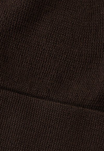 Gros plan d’un tissu tricoté brun foncé montrant des textures de points variées et un détail de couture diagonale.