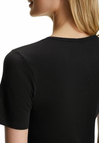 Maglietta nera a maniche corte con scollatura rotonda. Tessuto liscio con cuciture visibili lungo le cuciture. Design casual, taglio aderente.