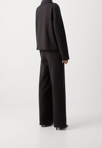 Czarny, prążkowany dwuczęściowy zestaw składający się z kwadratowej kurtki z kołnierzem oraz szerokich spodni. Materiał ma teksturowany wzór w paski.