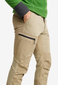 Beige outdoor pants with a side zip pocket, stitched detailing, and a logo. The material appears durable and wrinkle-resistant.