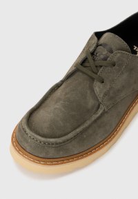 Olive green suede shoe with a rounded toe, featuring matching laces, a textured upper, and a contrasting tan rubber sole.