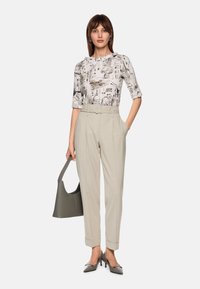 Light gray high-waisted trousers with pleats, paired with a patterned short-sleeve top in black and white, and gray leather handbag.