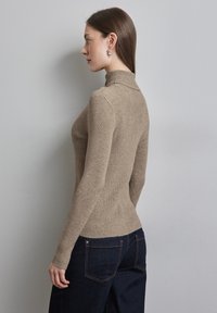 Beige gestreifter Rollkragensweater mit langen Ärmeln, enganliegendem Design und strukturiertem Stoff. Kombiniert mit dunkelblauen Jeans, von der Seite gezeigt.
