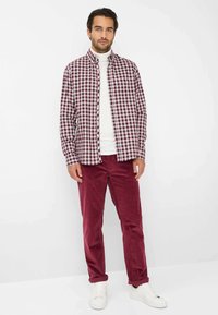 Geruite bordeauxrode en witte overhemddas, gedragen over een witte coltrui. Bordeauxrode corduroy broek en witte sneakers maken de outfit compleet.