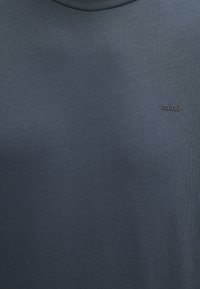 Marineblaue T-Shirt mit glatter Textur, runder Ausschnitt und kleinem schwarzen "mavi"-Logo auf der Brust.