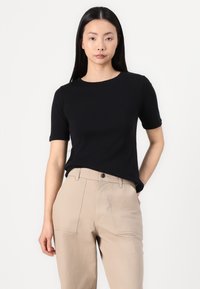 Maglietta nera a maniche corte con colletto rotondo, texture liscia. Abbinata a pantaloni beige chiaro a vita alta con due tasche frontali.