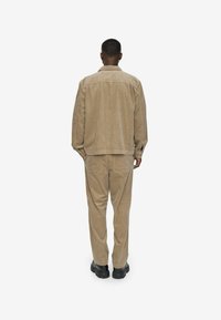 Beige corduroy jacket and matching trousers with a relaxed fit. The fabric has a textured surface, complemented by black footwear.