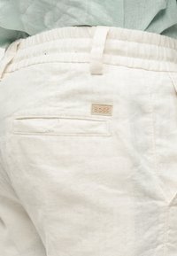 Κοντινό πλάνο λευκού παντελονιού με ελαστική μέση, πίσω τσέπη και ένα μικρό λογότυπο "BOSS" πάνω από την τσέπη.