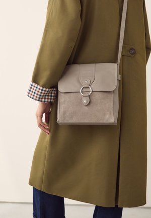 Szara torba na ramię z zamszu i skóry z płaską klapą, metalowym pierścieniem i subtelnym przeszyciem. W połączeniu z zielonym płaszczem i kratkowanym mankietem.