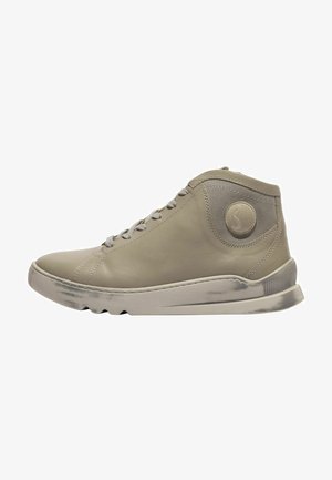 Zapatilla beige de caña alta con cordones en la parte delantera, puntera redondeada y parche circular con logo en el lateral, con suela ligeramente desgastada y costuras limpias.