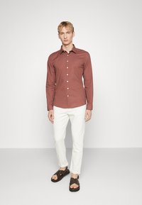 Piros mintás, hosszúujjú ing, gombos elülső résszel, fehér nadrággal és barna szandállal párosítva. Slim fit szabás és klasszikus gallér kialakítással rendelkezik.
