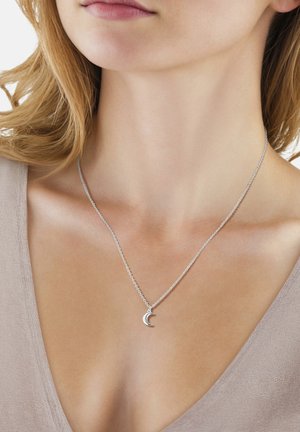 Silberner Halbmond-Anhänger an einer zarten Kette, getragen um den Hals einer Frau, die ein hellbeiges V-Ausschnitt-Oberteil trägt.