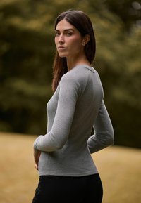 Graues, geripptes Langarmoberteil mit enganliegendem Design und Rundhalsausschnitt, kombiniert mit schwarzen Hosen. Weicher Stoff und feine Nähte.