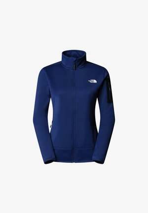 Chaqueta de forro polar azul marino con un cuello alto, cierre frontal con cremallera, dos bolsillos laterales y un bolsillo con cremallera en el brazo izquierdo. Presenta un logo en el pecho.
