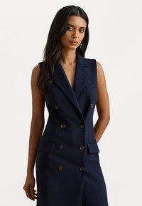 Marineblauw mouwloos dubbelgebreid vest met bruine knopen, reverskraag en twee voorzakken. Getailleerd ontwerp met een gladde textuur.
