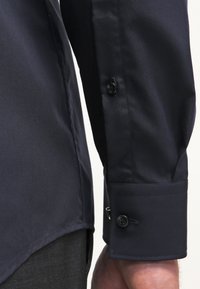 Marineblauwe longsleeve shirt met een gladde textuur, voorzien van dubbele knopen en een op maat gemaakte mouwontwerp. Rechte zoom zichtbaar.