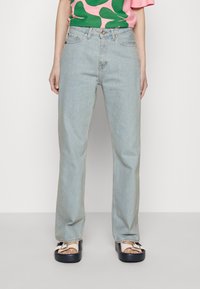 Jeans de pierna recta en azul claro con diseño de cinco bolsillos, que presentan un ligero desgaste y una textura clásica de denim; combinados con una blusa de patrón rosa y verde.