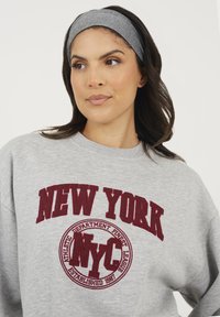 Felpa grigia con logo ricamato "NEW YORK" e "NYC" in color borgogna. Tessuto morbido, scollatura a girocollo, vestibilità ampia, maniche lunghe.