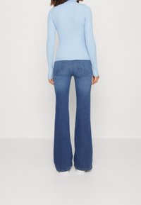 Lichtblauw geribbeld langslijfshirt met een strakke pasvorm, gecombineerd met donkerblauwe flared jeans met achterzakken en een gladde denim textuur.