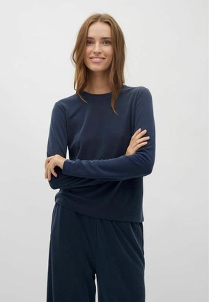 Navy lange mouwshirt van zachte stof, met een ronde hals en aansluitende mouwen. Model poseert met gekruiste armen, wearing bijpassende navy onderkleding.