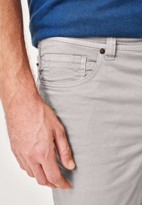 Light gray cotton pants with a smooth texture, featuring side pockets and a button closure, paired with a blue top. Hand positioned at the waist.