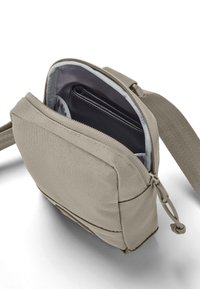 Lille beige crossbody taske med lynlås åben, der viser en sort pung indeni, på en hvid baggrund.