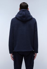 Giacca in fleece blu navy con una superficie testurizzata e pelosa, dotata di cappuccio e fondo dritto. Nessun sistema di chiusura o motivo visibile.