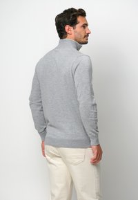 Grauer Pullover mit hohem Kragen, langen Ärmeln und tailliertem Design. Glatte Textur und Rippbündchen sowie Saumdetail.