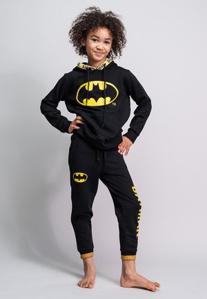 Schwarzes Hoodie- und Jogginganzug-Set mit gelbem Batman-Logo und Akzenten. Weiches Material, Pyjama-Stil mit gerippten Bündchen und Kordelzug.