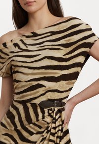 Asymetryczna sukienka bez ramiączek w beżowo-brązowe paski tygrysa, z marszczoną talią i ciemnobrązowym paskiem jako dodatkowym akcentem.