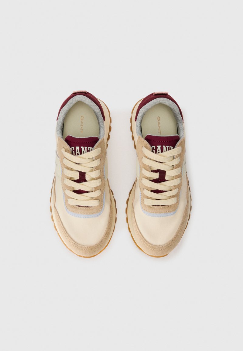 Ein Paar beige und kastanienbraune Sneaker mit cremefarbenen Schnürsenkeln, Gummisohlen und plüschigem grauem Innenfutter, von oben auf einem weißen Hintergrund betrachtet.