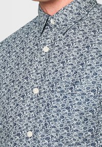 Skjorta med blommigt mönster i ljusblått med marinblå blommor, klassisk krage och en enkel bröstficka.