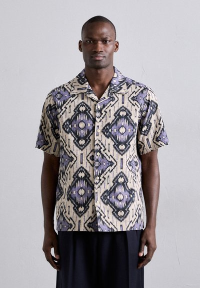 Short-sleeve button-up shirt in a cream and purple ikat pattern, featuring a collar and contrasting black accents, made from a lightweight fabric.
