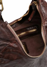 Interno di una borsa a tracolla in pelle marrone con una grande cerniera, caratterizzato da hardware in tonalità oro e diversi scomparti per organizzazione e archiviazione.