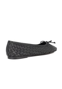 Black leather ballet flat with a woven texture, rounded toe, adjustable bow accent, and flat sole. Features a smooth finish and sleek design.