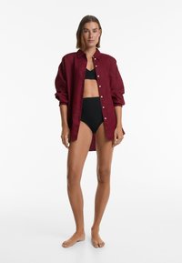 Burgundská lněná košile s uvolněným střihem, knoflíkovým zapínáním a dlouhými rukávy, spárovaná s černými bikinovými kalhotkami. Jednoduchý, čistý design.