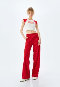 Pantalones anchos rojos con una textura suave y una cinturilla elástica, combinados con un top corto blanco que presenta mangas cortas rojas y texto impreso.