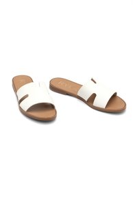 Sandali slide in pelle bianca con due cinghie a taglio, soletta color tan e suola piatta. Design semplice e texture liscia. Nessun dettaglio hardware visibile.