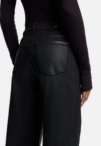 Jeans neri a vita alta con una texture liscia, due tasche posteriori e un sottile marchio vicino alla vita.