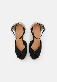 Sandali espadrilla neri in tela con design incrociato, dettagli del tacco in fibra naturale, cinturino regolabile e soletta marrone.