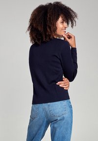 Pull en maille côtelée bleu marine avec un col rond et des manches longues, associé à un jean en denim bleu clair. Le tissu semble doux et texturé.