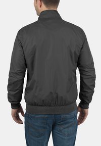 Schwarze Nylon-Bomberjacke mit geripptem Kragen und Taillenbund, ausgeführt in glatter Textur ohne sichtbare Logos oder Verzierungen.
