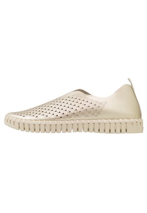 Zapatilla tipo slip-on en beige claro con un diseño de parte superior perforada y patrón texturizado. Cuenta con una suela gruesa con ranuras verticales para mayor tracción.