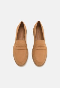 Tan semskede loafers med små broderte detaljer, rund tå, og en hevet stropp over det øvre partiet. Lett såle med teksturert finish.