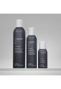 Drei schwarz-weiße Living Proof Perfect Hair Day Trockenshampoo-Flaschen in kleinen, mittleren und großen Größen auf einer grauen Oberfläche.