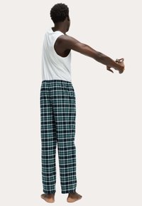 Heren pyjama's met een witte mouwloze shirt en groene geruite broek. De broek heeft een elastische tailleband en rechte pijpen.