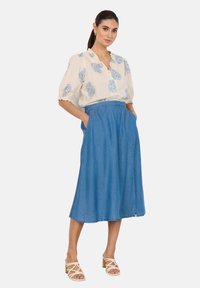 Blusa crema con estampado floral azul, mangas cortas y escote en V, combinada con una falda midi de mezclilla azul con bolsillos laterales y una silueta acampanada.