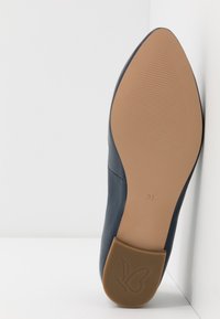 Chaussure en cuir marine avec un bout pointu et une semelle en caoutchouc marron. Présente des rainures texturées et un logo en forme de papillon sur le talon. Taille 37.