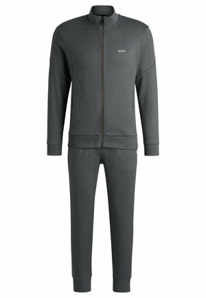 Tuta grigio scuro realizzata in tessuto morbido; presenta una giacca con zip e colletto alto e pantaloni con cerniere laterali. Inclusa una accentuazione con logo dorato.